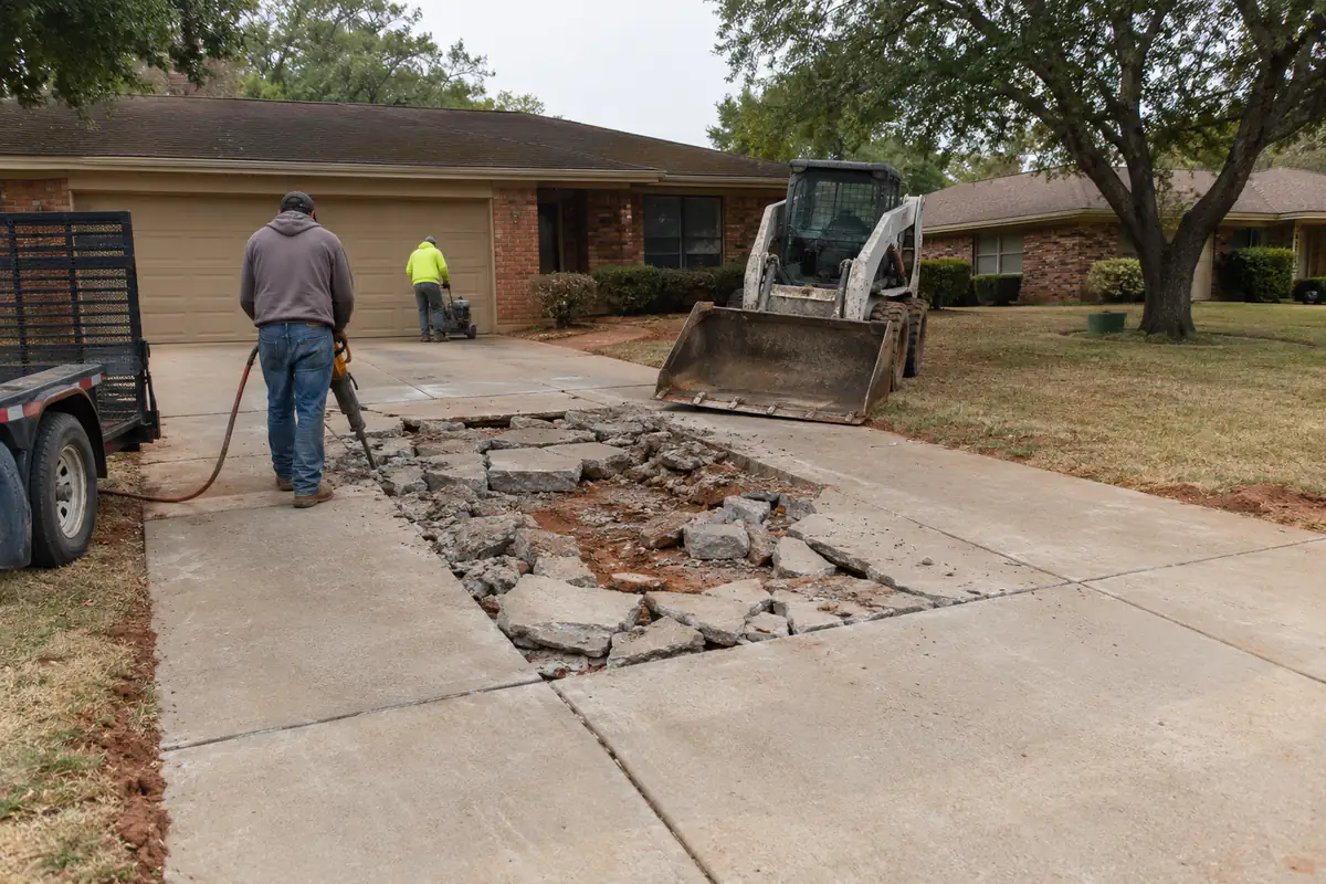 Before: A concrete driveway at a 1970s brick ranch house where one panel in the middle is shattered into pieces and sunken, the rest of the drive intact
