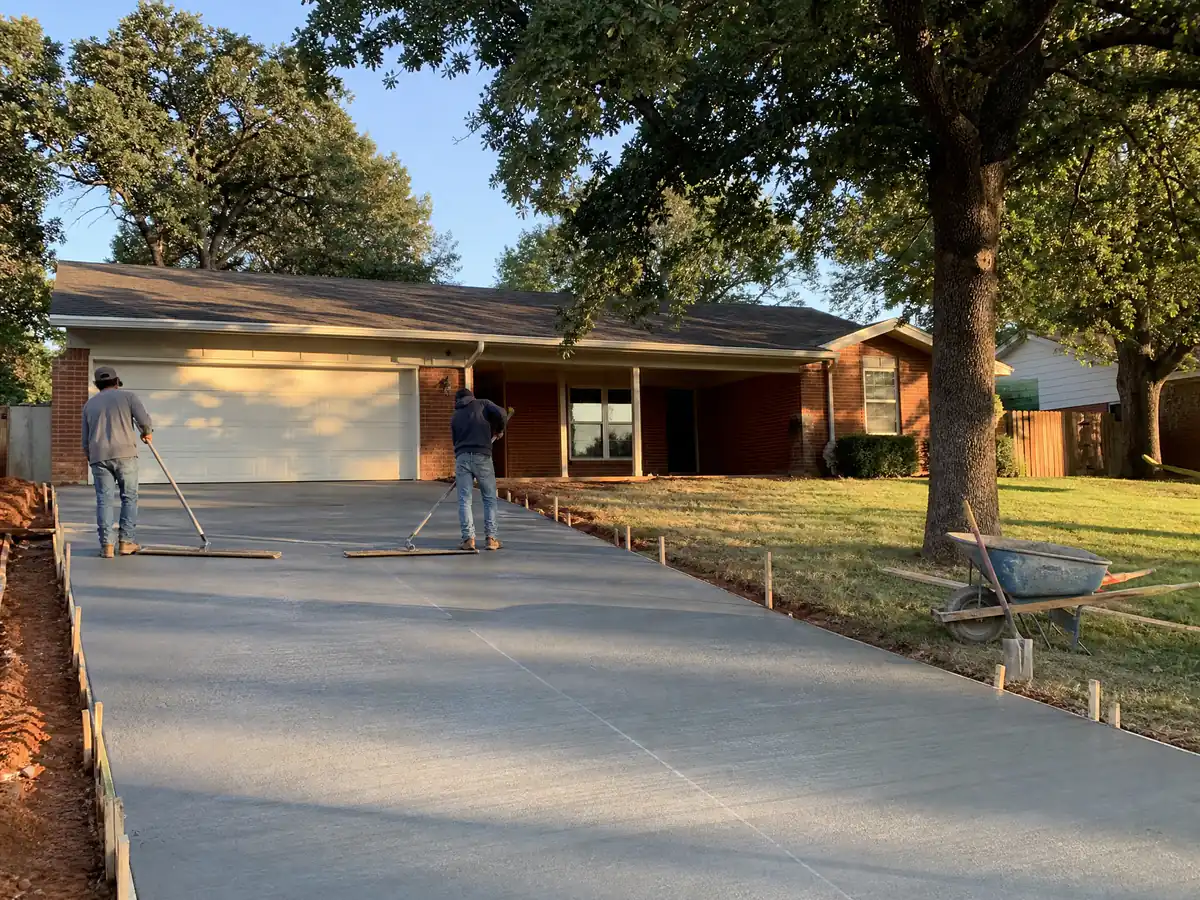 Crew broom-finishing a newly poured concrete driveway in front of a brick ranch house in Oklahoma City
