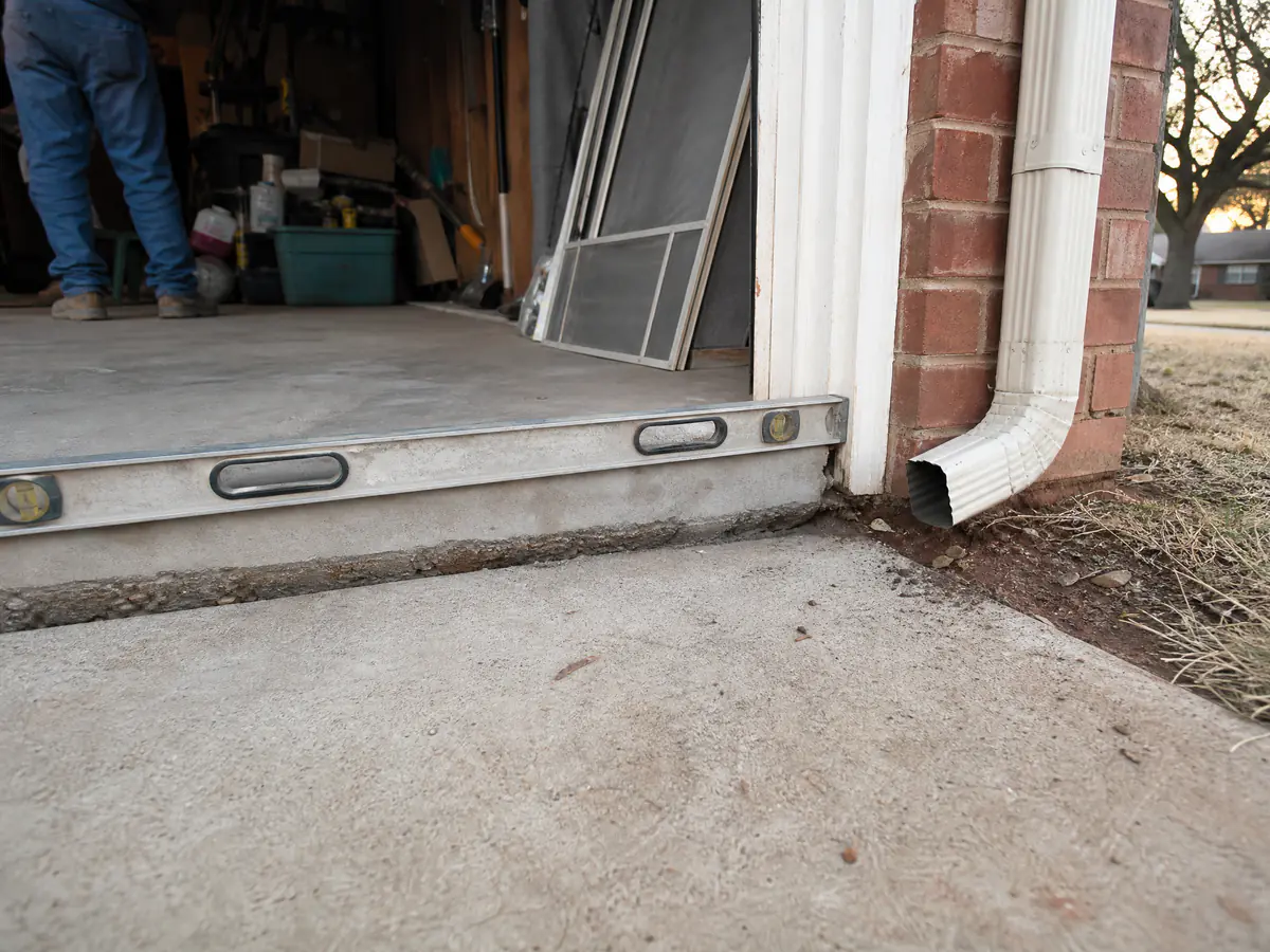 Concrete driveway dropped below the garage slab, with a level spanning the gap and a downspout nearby