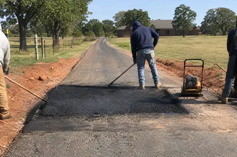 Crew raking hot asphalt into a full-depth patch on a long acreage driveway near Oklahoma City
