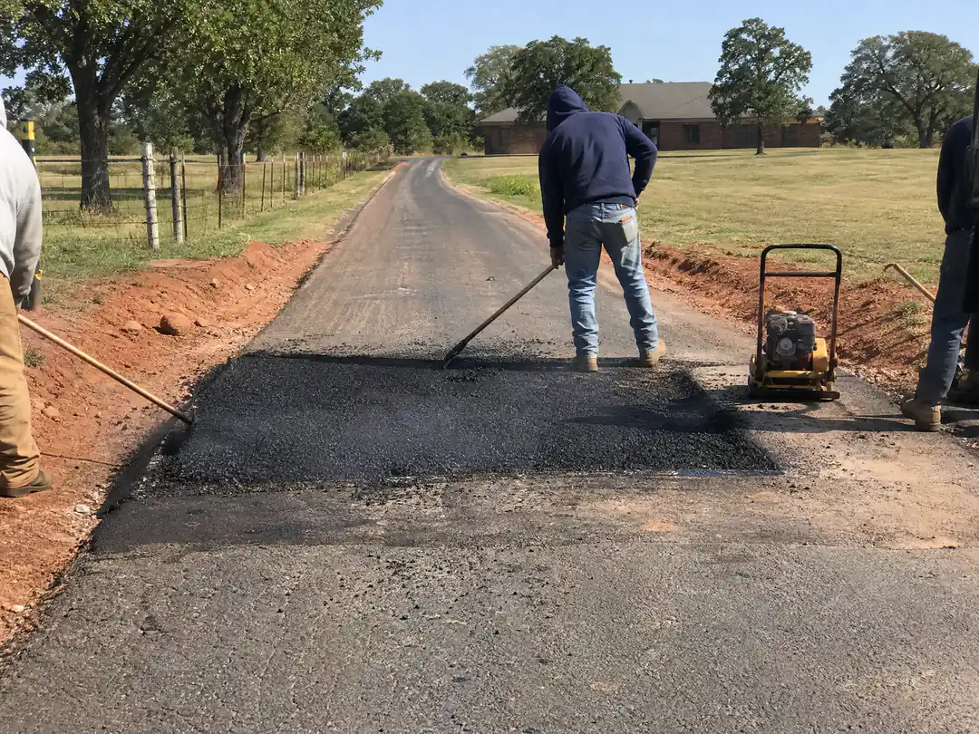Crew raking hot asphalt into a full-depth patch on a long acreage driveway near Oklahoma City