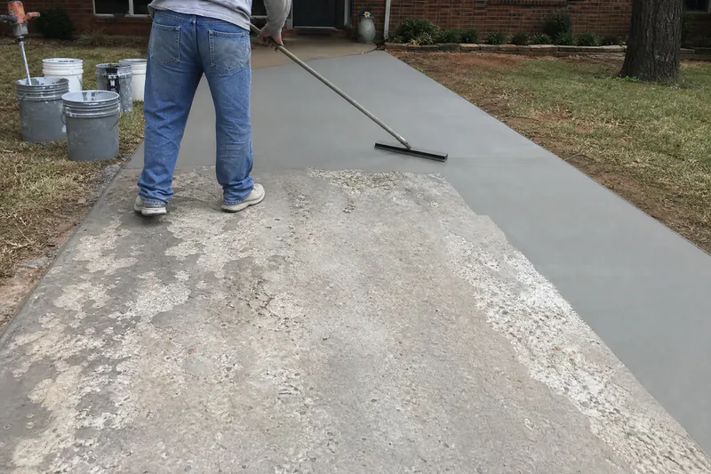 Worker squeegeeing a polymer-modified overlay across a scaled concrete driveway in Oklahoma City