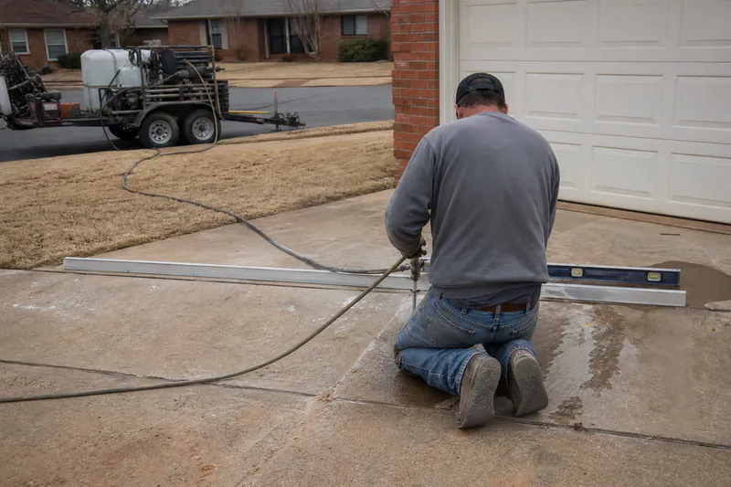 Technician injecting polyurethane foam through small drilled ports to lift a sunken concrete driveway in Oklahoma City