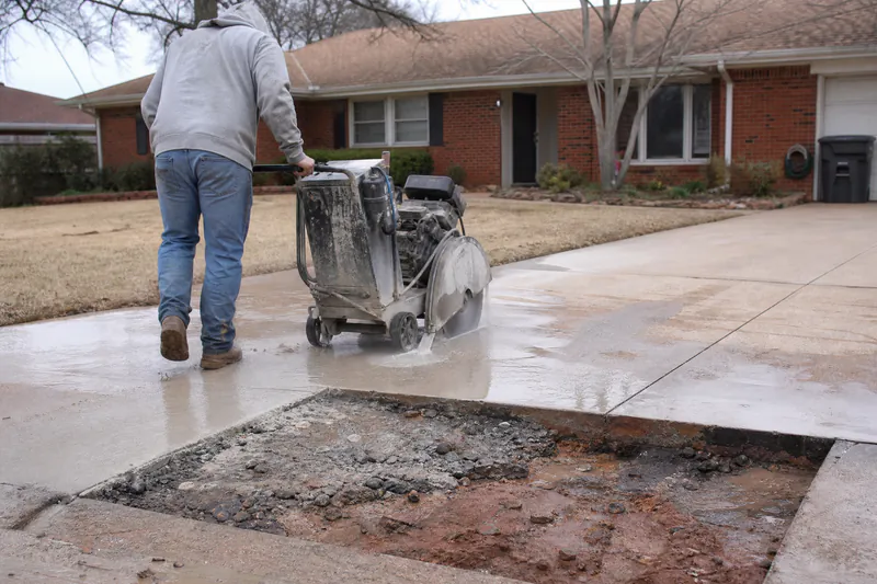Worker saw-cutting around a broken concrete driveway panel before removing it at an Oklahoma City home