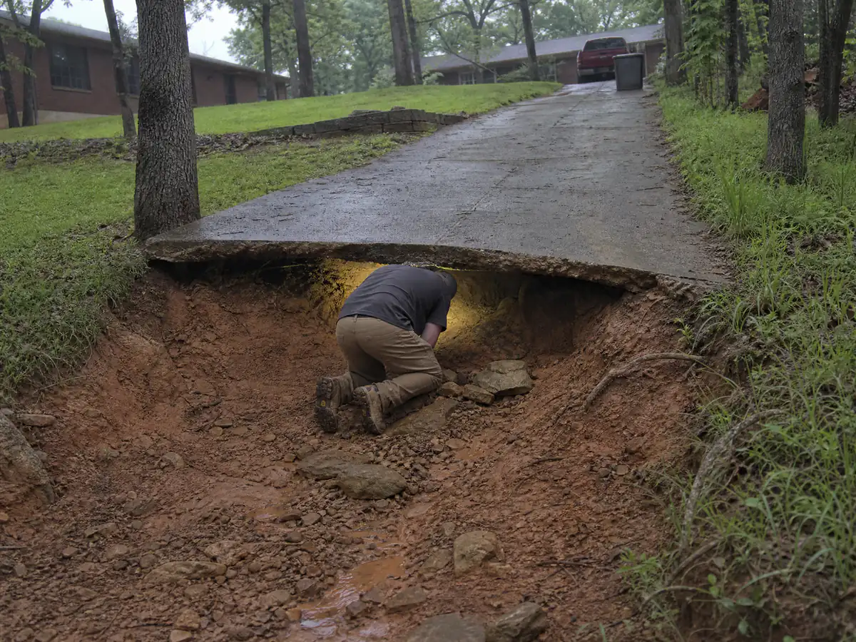 Runoff-carved void under the edge of a sloped concrete driveway on a hillside lot north of Oklahoma City